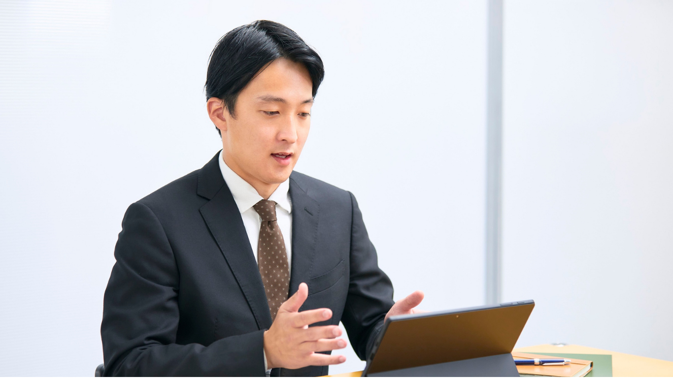Business professional in a suit speaking and gesturing while looking at a tablet during a meeting or virtual presentation. 